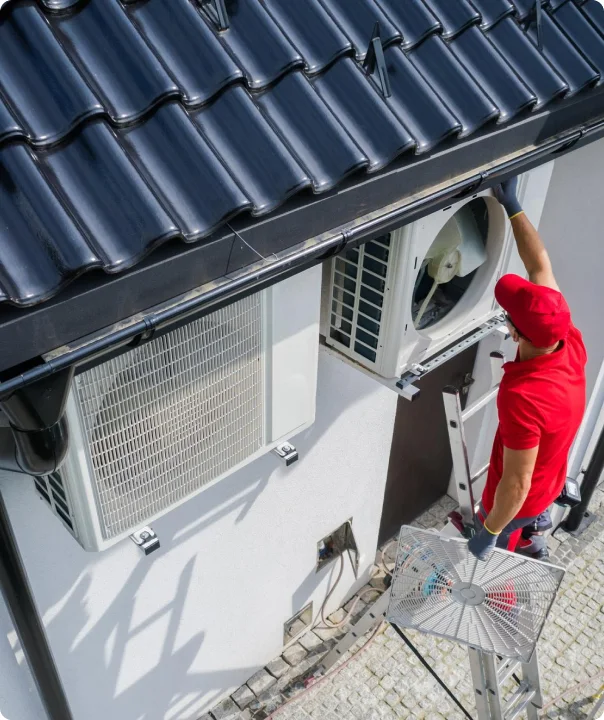Technician servicing outdoor air conditioning units beside a house