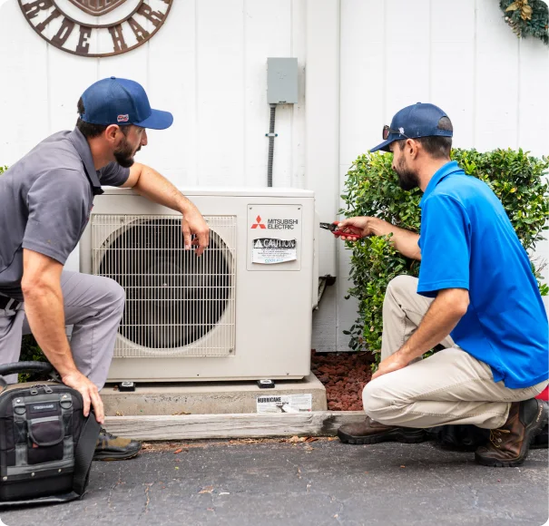 Two technicians servicing a Mitsubishi outdoor air conditioning unit