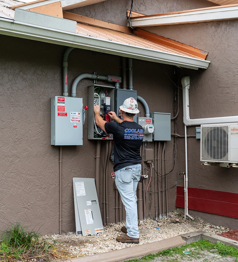 HVAC technician servicing an outdoor electrical panel and air conditioning system