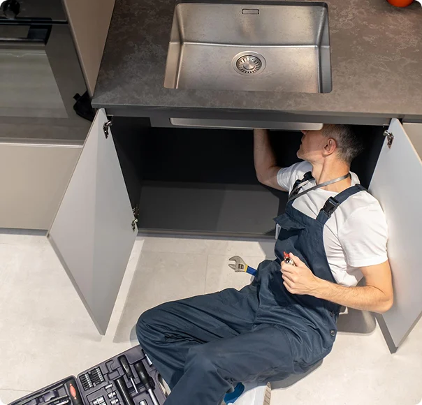 Plumber repairing pipes underneath a kitchen sink