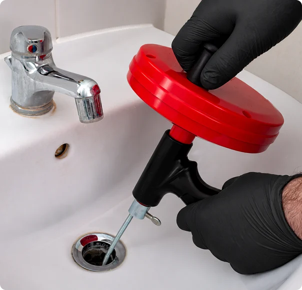 Plumber using a drain snake to clear a clogged bathroom sink drain.