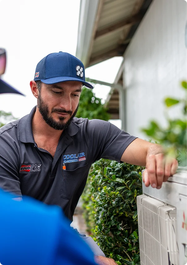CoolAir HVAC technician inspecting an outdoor air conditioning unit at a residential property.