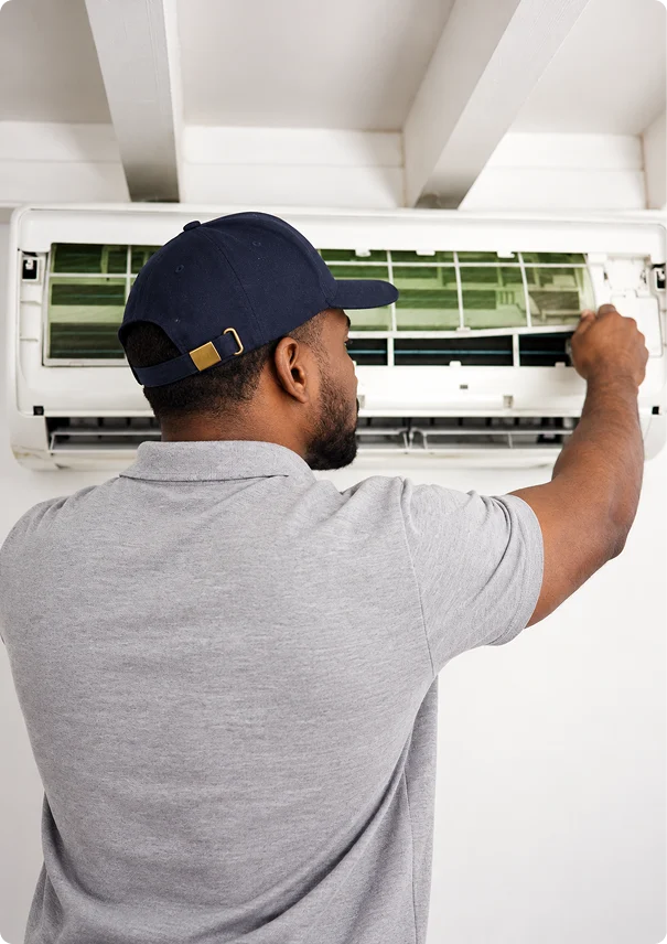 HVAC technician inspecting and cleaning the filter of a wall-mounted air conditioner.