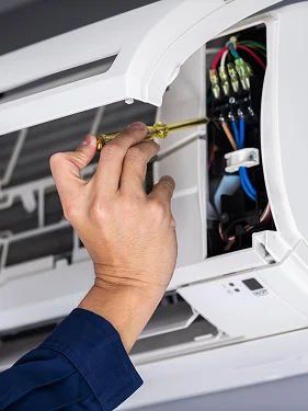 Close-up of an HVAC technician repairing the electrical components of an indoor air conditioning unit.