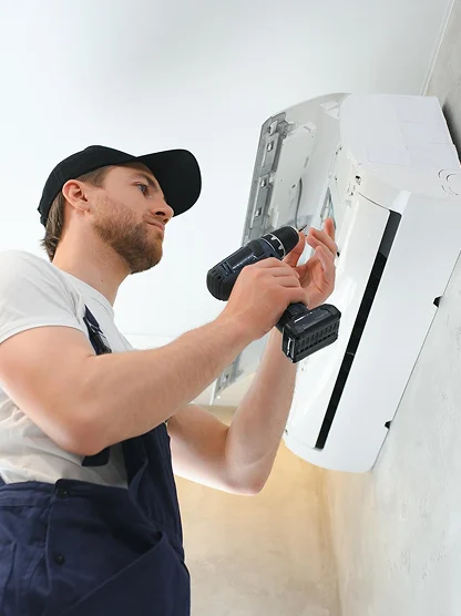 HVAC technician installing a wall-mounted ductless mini-split air conditioner using a power drill.