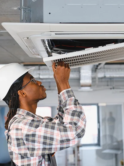 HVAC technician inspecting a ceiling-mounted air conditioning system in a commercial building.